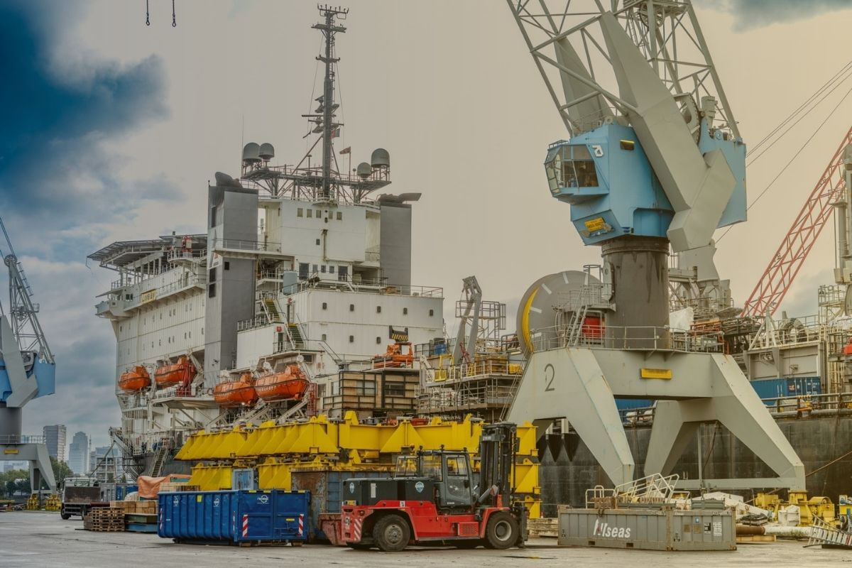 Uma cena portuária com um navio e guindastes operando na carga e descarga.