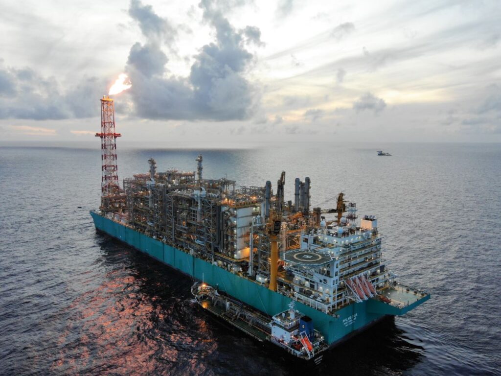 Uma embarcação de perfuração offshore com chamas saindo de uma torre, em um mar aberto.